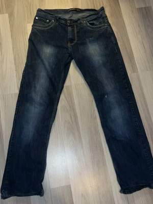 Armani byxor - Säljer ett par mörkblå jeans med raka ben och snygga slitningar framtill. Jeansen har klassiska fem fickor, kontrastsömmar och knappgylf. Materialet är denim i bomull. Perfekta för en avslappnad och trendig look.
