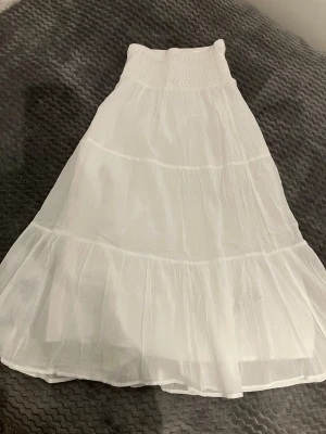 Vit långkjol från Gina Tricot storlek 146/152 i mycket bra skick. - Luftig och somrig vit långkjol från Gina Tricot med smock i midjan och volangdetaljer. Kjolen är tillverkad i bomull, passar perfekt för varmare dagar. Storlek 146/152 i mycket bra skick. 