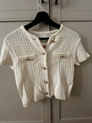 Vit kortärmad topp  - Vit kortärmad stickqd topp från H&M med guldknappar framtill.