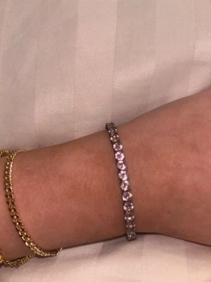 Silverfärgat armband med pärlor - Ett stilrent armband i silverfärg med gnistrande, runda pärlor längs hela bandet. Armbandet har justerbar kedja med små kulor i ändarna och passar perfekt för dig som gillar glittriga accessoarer. Materialet är metall och pärlorna har en kristall-liknande look.