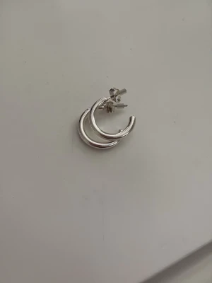 Silvriga hoops örhängen - Säljer ett par stilrena silvriga hoops örhängen. De är runda och har en blank finish som ger en modern vibe. Perfekta för dig som gillar minimalistiska accessoarer med lite extra attityd. Aldrig använda. Tror de är från glitter, hm eller Kappahl 