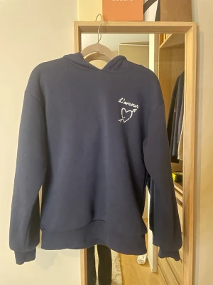 Mörkblå hoodie med L'amour-tryck från ginatricot  - Mörkblå hoodie med huva och vitt tryck på bröstet och ryggen där det står 'L'amour' tillsammans med ett hjärta och pil. Säljer då den inte passar mig❤️Orginalpris är ca 379kr skriv för mer bilder eller frågor( aldrig använd, endast testad )på bilden har jag ej ”trådar ” i luvan man det får man såklart med om man köper💕(på bilden är snörena i luvan borttagna men kommer så klart sättas tillbaka vid köp)💕