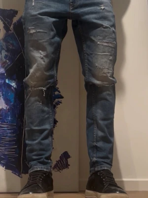 Blå slitna jeans från Icono - Säljer ett par blå jeans från Icono med snygga slitningar och trasiga detaljer på benen. Väldigt sköna och bra i storleken. Storlek 29/30! 