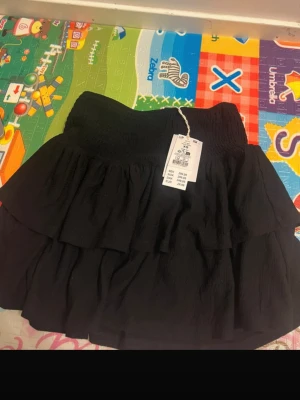 Svart volangkjol från GINA TRICOT - Svart kortkjol från GINA TRICOT  med flera lager volanger och smockad midja. Strl XS, helt oanvänd. Perfekt för sommaren! Pris går att diskutera