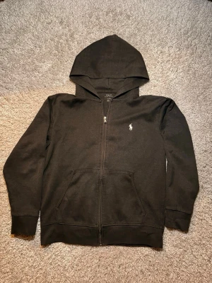 Svart hoodie från Polo Ralph Lauren - Svart hoodie med dragkedja från Polo Ralph Lauren. Mjuk bomullskvalitet som är skön att ha på sig. Storlek M, pm för mer info