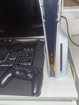 PlayStation 5 med svart handkontroll - PlayStation 5 konsol i vit och svart design med en tillhörande svart DualSense handkontroll. Konsolen har en futuristisk form och är tillverkad i plast med en matt och blank finish. Perfekt för gaming och upplevelser i hög kvalitet.