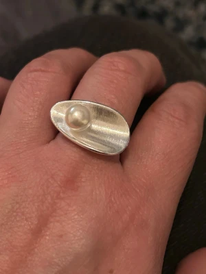 Modern silverring med pärla - Snygg och unik ring i silver med en stor, oval formad platta och en vit pärla centrerad på ovansidan. Ringen har en borstad yta som ger en cool, modern känsla. Perfekt för dig som gillar statement-smycken och vill sticka ut. Edblad. Pilgrim. Ioaku. Syster p. Zara  Gina tricot. 