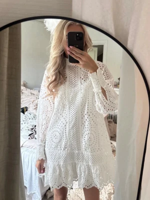 Vit broderad kort klänning - Säljer en vit kort klänning med broderade detaljer och volangkant. Klänningen har långärmade ärmar med knyt vid handlederna och är tillverkad i ett luftigt bomullstyg. Perfekt för sommarens alla tillfällen!🫶🏻