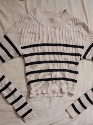 Beige stickad tröja med svarta ränder - Trendig beige stickad tröja med svarta horisontella ränder. Tröjan har ribbad struktur, rund halsringning och långa ärmar. Perfekt för dig som gillar en enkel men snygg look. Passar till både jeans och kjol.