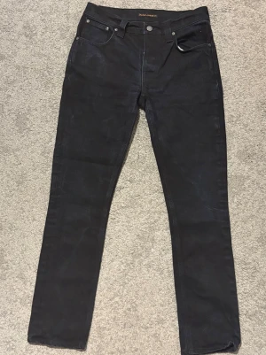 Nudie Jeans 31/32 - Säljer ett par svarta jeans, med blåa drag, från Nudie Jeans med slim straight passform, modell Grim Tim. Sköna och stilrena jeans. Storlek W31 L32. Hör av dig vid frågor.