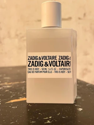 Zadig & Voltaire This Is Her! EdP 50ml - Minimalistisk parfymflaska i matt vit glas från Zadig & Voltaire. Modellen heter This Is Her! och rymmer 50 ml Eau de Parfum. Flaskan har en stilren, fyrkantig form med svart text på vit etikett och en matchande vit kork.