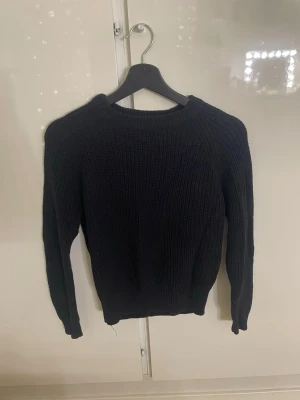 Svart stickad tröja med rund hals - Storlek S men jag skulle säga att den är lite liten i storlek. Använd ett fåtal gånger. En enkel och stilren svart stickad tröja med rund halsringning och långa ärmar. Tröjan har ribbstickade muddar vid ärmslut och nederkant.