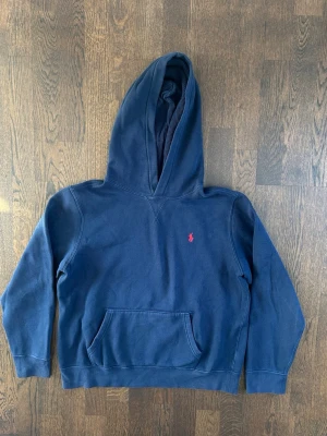 Ralph Lauren Fleece Hoodie Kids Blue - Klassisk mörkblå hoodie från Polo Ralph Lauren med huva och magficka. Tröjan har en liten röd broderad logga på bröstet och är tillverkad i mjuk bomull. Nypris : ca 1300 SEK pris : 399 SEK