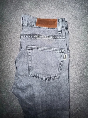 Gråa jeans från Woodbird - Snygga gråa jeans från Woodbird med klassisk femficksdesign och läderpatch bak i midjan. Jeansen har en smal passform och är tillverkade i ett mjukt denimtyg. Perfekta för en trendig och avslappnad stil. Orginal pris 999kr. 28/32