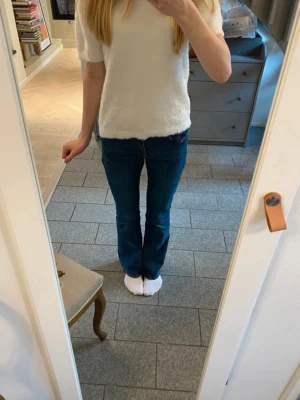 Mörkblå bootcut jeans - Säljer ett par mörkblå bootcut jeans med klassisk femficksdesign och normalhög midja. Jeansen har en lätt utsvängd passform nertill och är tillverkade i ett stretchigt denimtyg som sitter snyggt på kroppen.