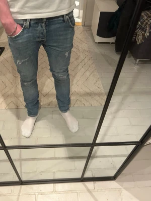 Slim fit ljusblå slitna jeans  - Säljer ett par slim fit ljusblå jeans med slitningar på knäna och lätt tvättad look i storlek 29/30. Jeansen har klassisk femficksmodell och smal passform som sitter snyggt längs benen. Perfekta för en avslappnad och trendig stil.