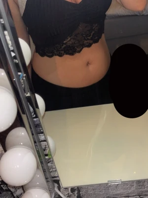 Svart croppad spets topp - Snygg svart croppad topp med omlott och spetsdetaljer nertill. Toppen är ärmlös och har en feminin, trendig look som passar perfekt till höga jeans eller kjol. Storlek är oklart men skulle säga S/M. 