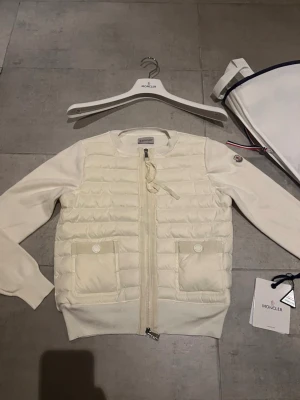 Moncler cardigan dam vit - Hej! Jag säljer nu min jättefina Moncler cardigan. Cardiganen är i jättebra skick och har inga defekter eller liknande skicket 9,5/10. Den är äkta och köpt online. Jag säljer den pågrund av att den inte riktigt passar min personliga stil. Moncler dustbag lapprna osv ingår med jackan. Hör av dig vid minsta lilla fråga! 💕