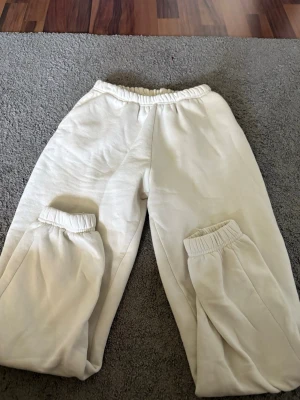 Vita mjukisbyxor från Gina Tricot - Säljer ett par vita mjukisbyxor från Gina Tricot, modellen 'basically basic'. Byxorna har resår i midjan och vid bensluten för en skön och avslappnad passform. Perfekta för chill dagar hemma eller när du vill vara bekväm. Tillverkade i mjukt material.