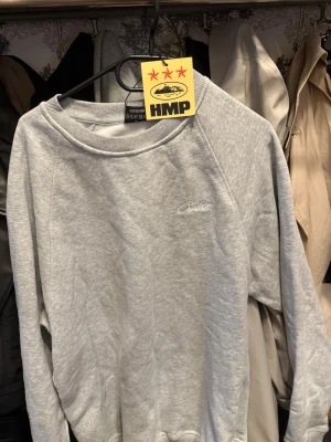 Corteiz Sweatshirt - Snygg grå crewneck från Cortiez med broderad logga på bröstet. Tröjan har rund halsringning, långa ärmar och ribbade muddar vid ärmslut och nederkant. Perfekt för en avslappnad och stilren look.