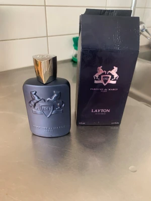 Parfums de Marly Layton EdP 125ml - Säljer en lyxig parfym, Layton Eau de Parfum från Parfums de Marly. Flaskan är matt mörkblå med silverfärgad kork och har en elegant relief med två hästar och sköld. Kommer i originalkartong. Volym: 125 ml.