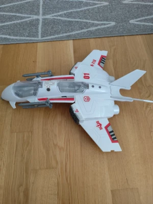 Vit leksaksjet med röda detaljer - Coolt leksaksflygplan i vit plast med röda och svarta detaljer samt genomskinlig cockpit. Modellen har två missiler på vingarna och tryckta siffror och symboler. Perfekt för dig som gillar action och flygplan.
