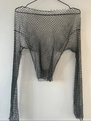 Svart mesh topp med lång ärm - Cool svart mesh topp med lång ärm och vid halsringning. Tunt, genomskinligt nätmaterial som ger en edgy vibe och passar perfekt till lager-på-lager-stil. Snygg att styla över linne eller bralette.