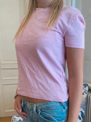 Ljusrosa topp - Snygg ljusrosa t-shirt i bomull med korta ärmar och rund halsringning. Modellen är rak och passar perfekt till jeans eller shorts. T-shirten har en clean look utan tryck eller mönster. 💗💗