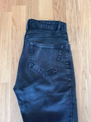 Svarta raka jeans från Lindex - Snygga svarta jeans från Lindex med raka ben och klassisk femficksmodell. Jeansen har hög midja, bälteshällor och silverfärgad knapp. Perfekta för en trendig och avslappnad look.