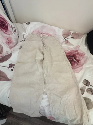Beiga vida linnebyxor med dragsko från H&M  - Snygga och luftiga linnebyxor i beige med bred passform och elastisk midja med dragsko. Perfekta för en avslappnad stil och sköna varma dagar. Tillverkade i linne för en naturlig och sval känsla.