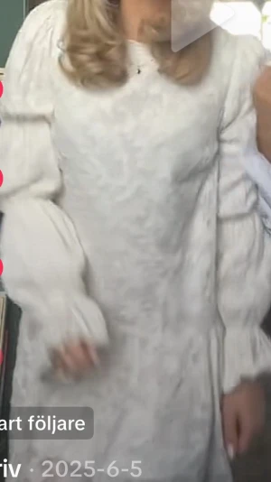 Vit långärmad klänning med puffärm - Elegant vit klänning med subtilt blommönster och långa puffärmar. Klänningen har en rak passform och är tillverkad i ett tyg som ser ut som bomull eller polyester. Perfekt för dig som gillar romantiska detaljer och stilren design.