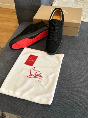 Svarta sneakers från Christian Louboutin - Snygga svarta sneakers från Christian Louboutin med klassisk röd sula. Skorna har en stilren design i mocka och läder, svarta skosnören och diskreta detaljer. Perfekta för dig som vill ha en lyxig och trendig look med ikonisk touch.