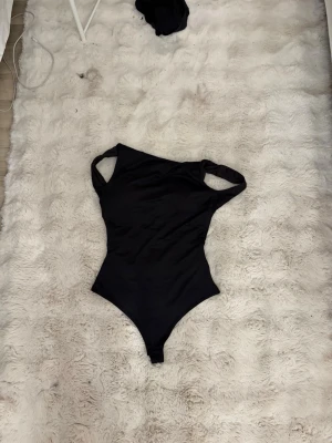 Svart festbody med breda axelband - Snygg svart festbody med breda axelband och rundad halsringning. Tight passform som framhäver figuren och klassisk design utan synliga detaljer. Perfekt att styla till olika outfits. Materialet känns stretchigt och bekvämt.