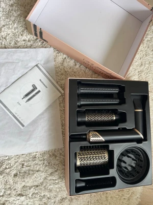 Multistyler för hår med flera tillbehör - Säljer en svart och guldig multistyler för hår med flera utbytbara tillbehör, inklusive rundborstar, volymmunstycke och diffuser. Allt ligger i originalförpackning med instruktionsmanual. Perfekt för att styla håret på olika sätt.