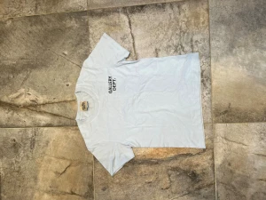 Vit t-shirt från Gallery Dept. - Snygg vit t-shirt från Gallery Dept. med svart tryck på bröstet. Klassisk rund halsringning och korta ärmar. Perfekt för en clean och stilren look. Tillverkad i mjuk bomull som känns skön mot huden.