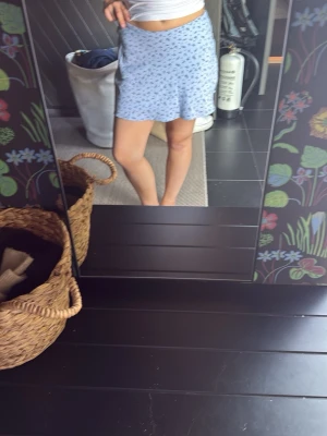 Blå kortkjol med blommigt mönster - Säljer en ljusblå kortkjol med små blommor. Kjolen har en lätt utsvängd form och är perfekt för dig som gillar en söt och avslappnad stil. Materialet känns mjukt och bekvämt, och kjolen har en normal passning som sitter snyggt på höften.
