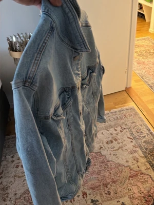 Ljusblå jeansjacka från Zara - Snygg ljusblå jeansjacka från Zara med klassisk passform. Jackan har två bröstfickor med lock och knappar samt tydliga sömdetaljer. Perfekt för dig som vill ha en tidlös och trendig look.