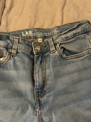 Ljusblå raka jeans från LAB Industries - Ljusblå jeans från LAB Industries i rak modell med klassisk femficksdesign och bälteshällor. Jeansen är tillverkade i hållbar denim och har en avslappnad passform som är perfekt för en chill och trendig look.