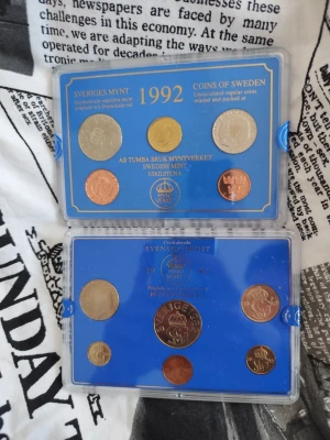 Svenska myntset 1992 och 1993 - Två kompletta svenska myntset från 1992 och 1993 i originalförpackning. Mynten ligger i blå plastaskar med genomskinligt lock och innehåller olika valörer i silver-, guld- och kopparfärg. Perfekt för samlare av svenska mynt.