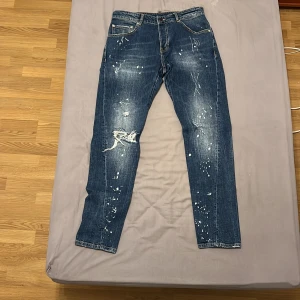 Blå jeans från Dsquared2 - Snygga blå jeans från Dsquared2 med slitna detaljer och färgstänk för en cool look. De har en klassisk femficksdesign och knappgylf. Perfekta för en avslappnad stil med en touch av edge.