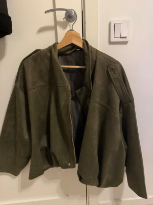 Olivgrön oversized skinnjacka - Snygg olivgrön skinnjacka med avslappnad, oversized passform och dragkedja framtill. Jackan har breda axlar och en minimalistisk design utan synliga fickor eller detaljer. Perfekt för en cool och trendig look.