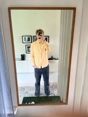 Ljusgul skjorta i bomull - Säljer en ljusgul skjorta i bomull med klassisk krage och långa ärmar. Skjortan har knappar framtill och en relaxed passform som ger en chill vibe. Perfekt att styla med jeans eller chinos för en clean look.