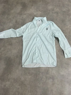 Ljus grön skjorta från Ralph Lauren - Klassisk Ljus grön från Ralph Lauren med lång ärm och knappar framtill. Skjortan har den ikoniska loggan broderad på bröstet och är tillverkad i ett mjukt bomullstyg. Perfekt för en clean och stilren look. Pris går och diskutera bästa looken för skolavslutning eller nått annat.