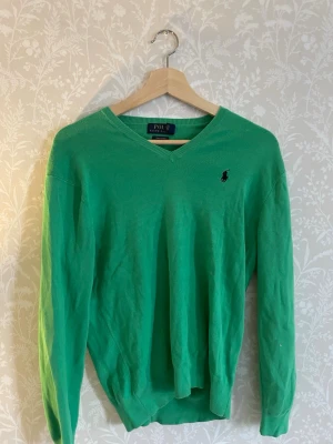 Grön v-ringad tröja från Polo Ralph Lauren - Snygg grön tröja från Polo Ralph Lauren i mjuk pima cotton. V-ringad modell med klassisk broderad logga på bröstet. Perfekt för dig som gillar stilrena och tidlösa plagg. Långa ärmar och ribbade muddar.