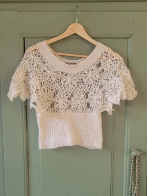 Vit stickad topp - Säljer en vit, kortärmad stickad topp med virkat mönster upptill och ribbstickad nederdel. Toppen har bred halsringning och luftig design, perfekt för lager på lager. Materialet känns mjukt och lätt. Så fin och sitter åt i midjan!