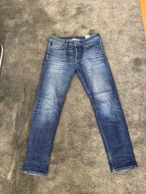 Blå slim fit jeans med slitningar - Snygga blå slim fit jeans med lätt slitna detaljer och klassisk femficksdesign. Jeansen har en något tvättad look och raka ben. Perfekta för en avslappnad och trendig stil. Storlek 31/32