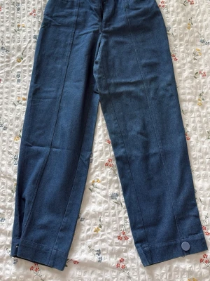 Caro Editions Cargo Denim – Size XS - Säljer ett par blå jeans med raka ben och hög midja. Jeansen har en snygg knappdetalj längst ner på benen och markerade sömmar framtill. Materialet är klassisk denim som känns både slitstarkt och bekvämt. Perfekta för dig som gillar en clean och stilren look.