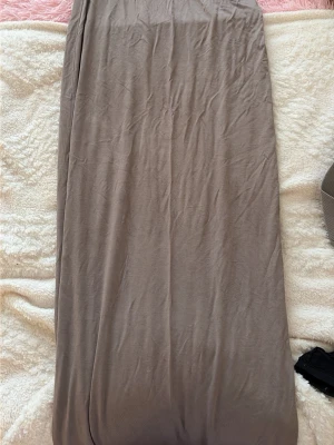 Beige långkjol i mjukt material - En enkel och stilren beige långkjol i ett mjukt och följsamt material. Kjolen har en rak passform och passar perfekt till både sneakers och sandaler. Snygg att matcha med en crop top eller en stickad tröja.