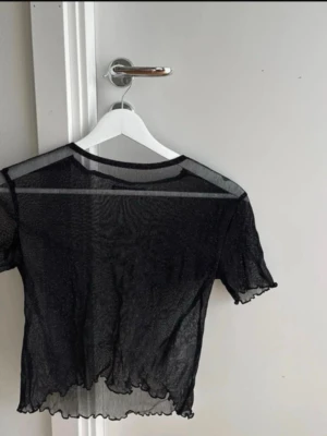 Svart mesh topp från Brandy Melville -  en svart, glittring mesh topp från Brandy Melville. Toppen har korta ärmar, croppad passform och vågig kant nertill. Perfekt att styla lager på lager för en trendig look.