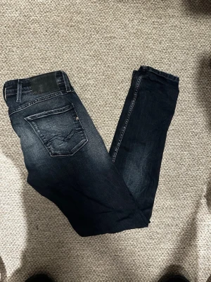 Mörkblå Replay jeans med slitningar - Snygga mörkblå jeans från Replay med slim fit-passform och slitna detaljer på framsidan. Jeansen har klassiska fem fickor, tydliga sömmar och en läderpatch bak i midjan. Perfekta för en trendig och avslappnad look. Kan gå ner i pris vid smidig och snabb affär.